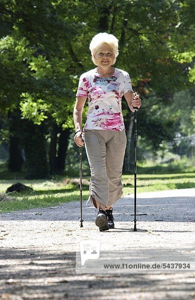 a elderly woman is walking in a park with walking staves