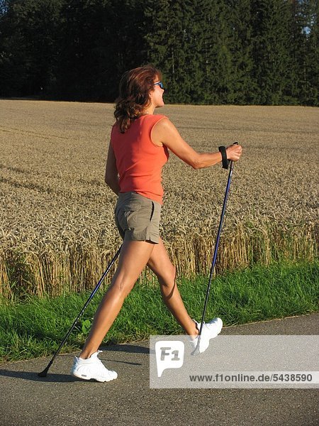 A Woman with the Nordic Walking goes next to a cornfield on an asphalted country lane.