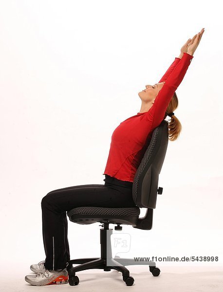 fit im Büro - junge Frau sitzt auf Bürostuhl und macht Gymnastik - Arme über den Kopf strecken - Beweglichkeit