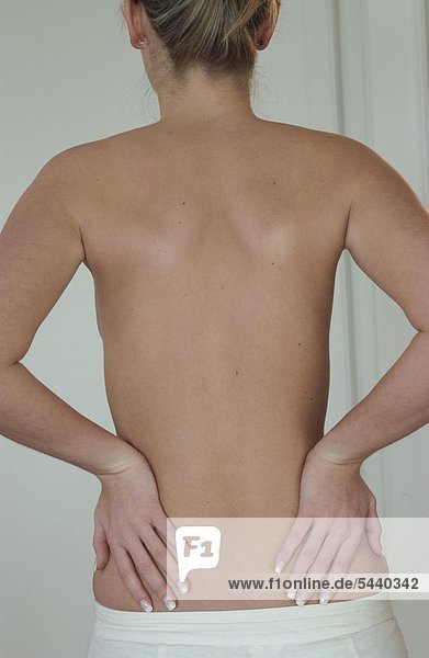 Halbtotale - Rückenansicht von junger schlanker Frau mit Rückenschmerzen