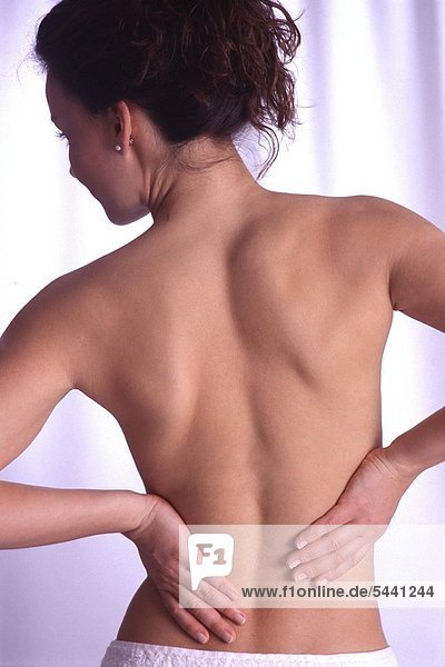 Rückenansicht - Junge Frau hält sich mit beiden Händen den Lendenwirbelbereich