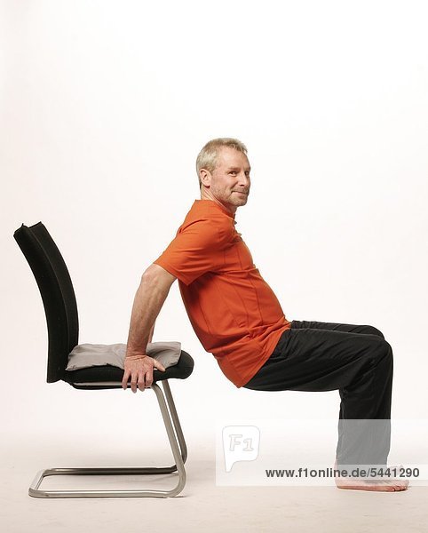 older man resting with both hands backwards on a chair - sole of feet are in front of the chair - he is pushing his body with his arms up and down - training of the arm muscles