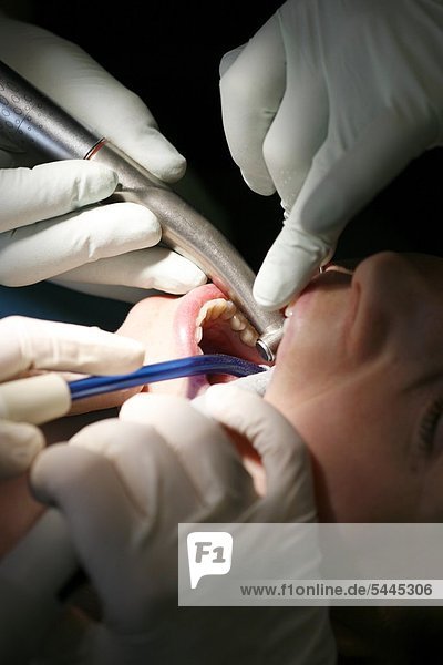 Zahnarztpraxis : Zahnarzt und Zahnarzthelferin behandeln einen Patienten mit Bohrer und Absauger