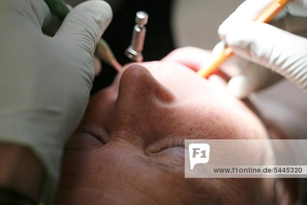 Zahnarztpraxis : eine Patientin wird von einem Zahnarzt oder einer Zahnärztin mit einer Sonde und einem Mundspiegel behandelt.