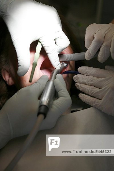 Zahnarztpraxis : Zahnarzt und Zahnarzthelferin behandeln einen Patienten mit Bohrer   Absauger und Sonde