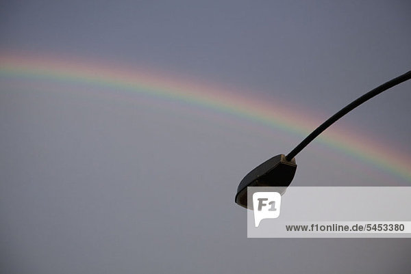 Ein Regenbogen im Rücken einer silhouettierten Straßenlampe