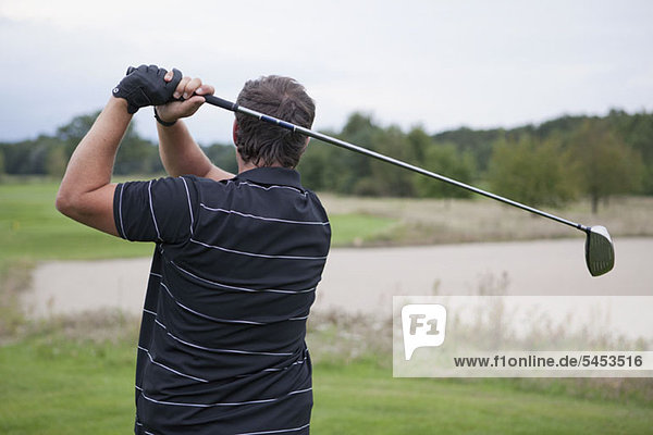 A golfer teeing off  rear view  waist up
