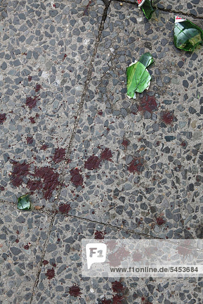 Eine zerbrochene Bierflasche und gespritztes Blut auf einem Bürgersteig.