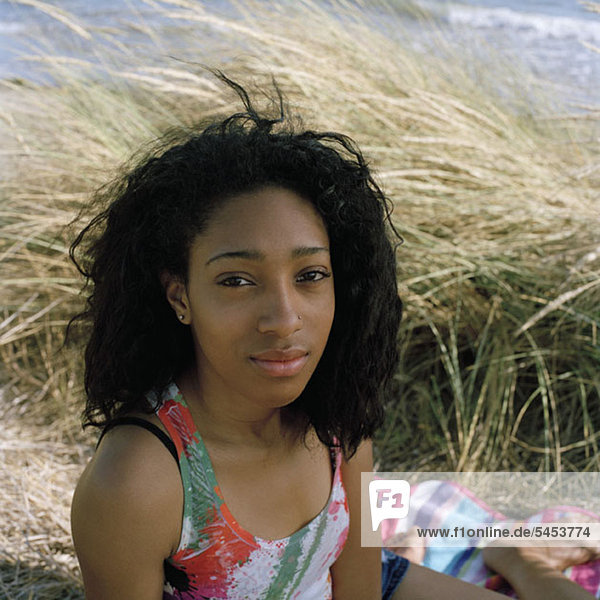 Ein Teenager-Mädchen sitzt am Strand und schaut in die Kamera.