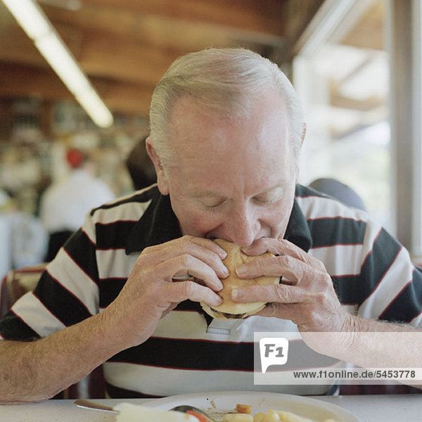 A senior man eating a hamburger