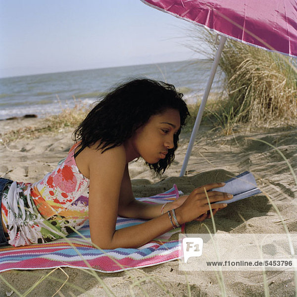 A teenage girl lying on the beach reading a book