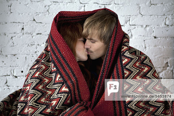 Ein junges Paar in eine Decke gewickelt  die sich küsst.