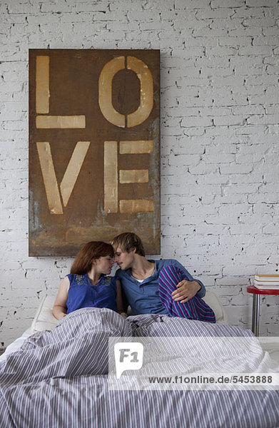 Ein junges Paar liegt im Bett und will sich küssen.