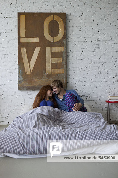 Ein junges  grinsendes Paar im Bett  das sich auf einen Kuss vorbereitet.