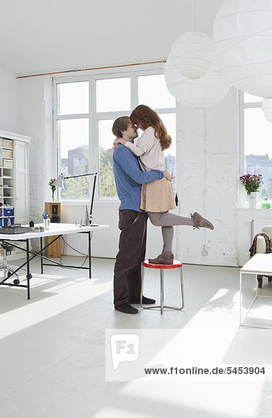 A woman standing on a stool with her arms around her boyfriend