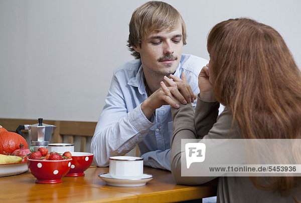 Ein junges Paar hält sich am Frühstückstisch an den Händen.