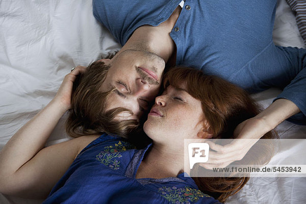 A young couple lying head to head on a bed  eyes closed