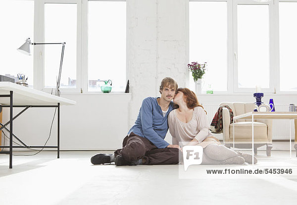 Ein junges  liebevolles Paar sitzt Seite an Seite auf dem Boden.