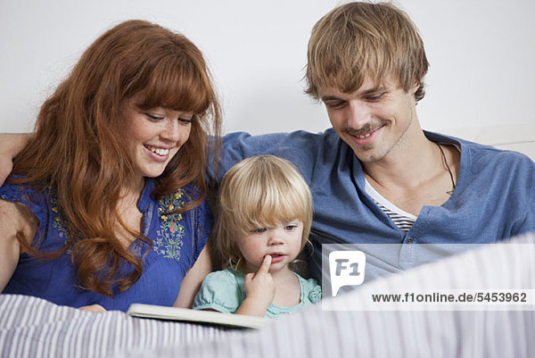 Eine junge Familie beim Lesen eines Bilderbuches im Bett