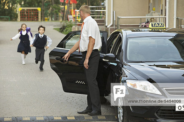 Two children in school uniforms running towards black cab