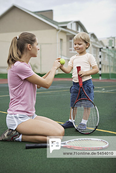 Eine Mutter  die ihrem kleinen Sohn Tennis beibringt.