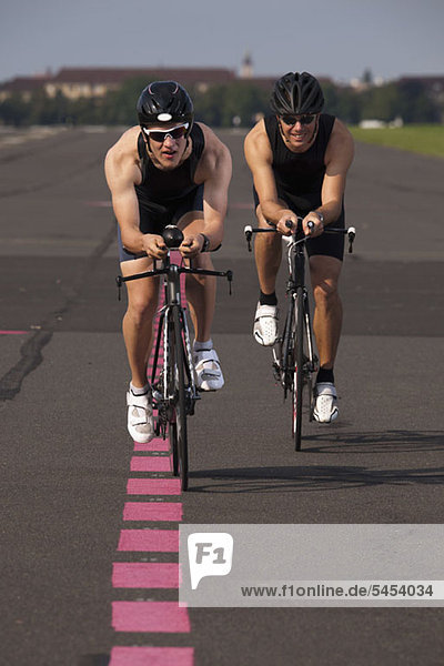 Zwei Radfahrer auf Rennrädern  die auf einer markierten Straße radeln.