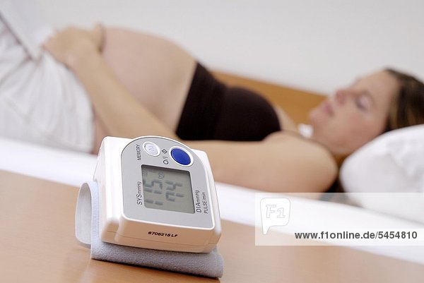 Nackte schwangere Frau schläft mit Blutdruckmeßgerät