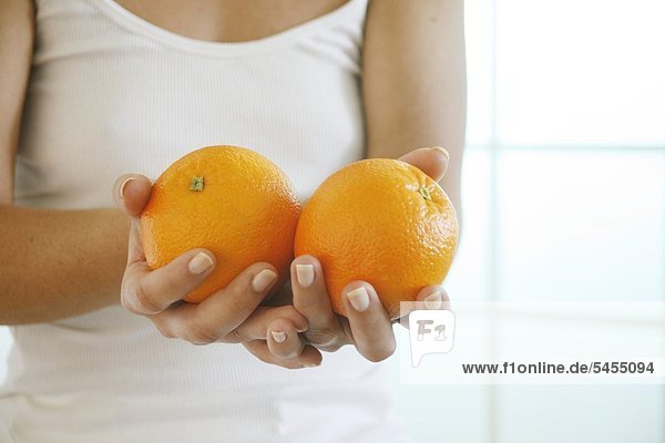Weibliche Hände halten zwei Orangen.