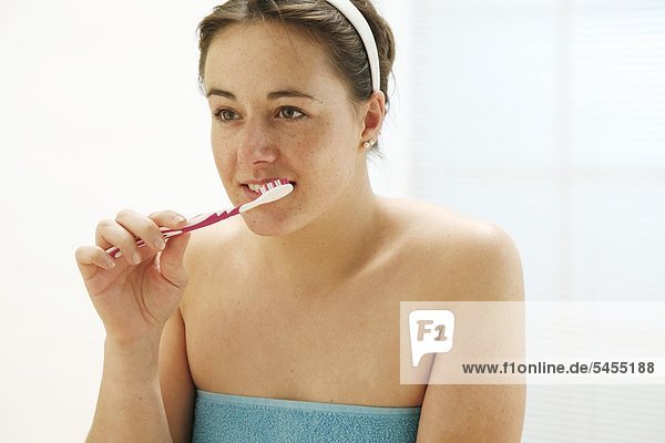 junge Frau bekleidet mit einem Handtuch putzt sich die Zähne mit Zahnbürste