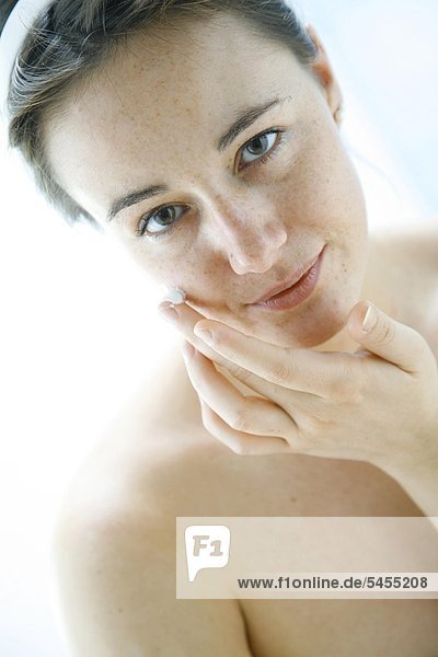 portrait einer jungen Frau die sich das Gesicht mit Gesichtscreme eincremt