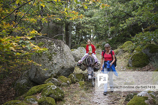 Mother and daughter walking with a donkey during a family-hike with a donkey in the Cevennes Mountains  France  Europe