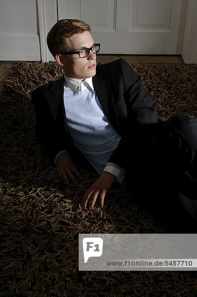 Junger Mann mit Brille und Anzug  auf Boden liegend