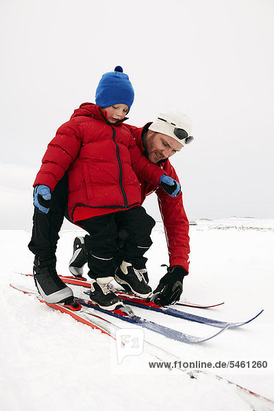 Man helping child put on skis in snow