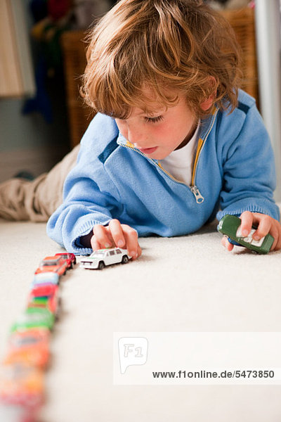 Young boy lining up toy cars in his bedroom