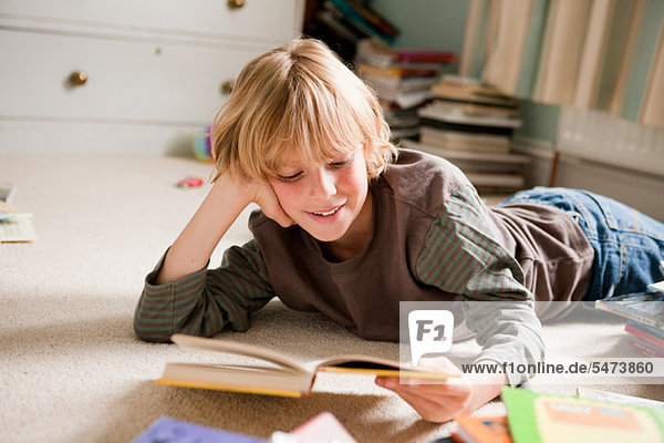 Kleiner Junge  der auf seiner Vorderseite liegt und ein Buch in seinem Schlafzimmer liest.