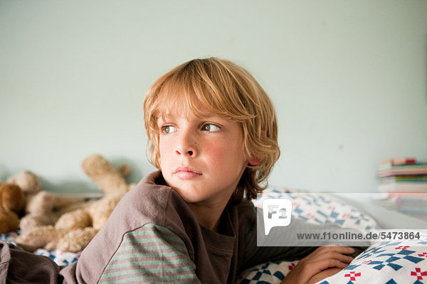 Young boy lying on bed staring into distance