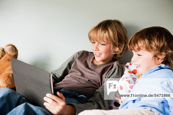 Two young boys on a bed  using a digital tablet