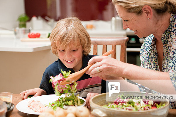 Mother serving salad to son at dining table