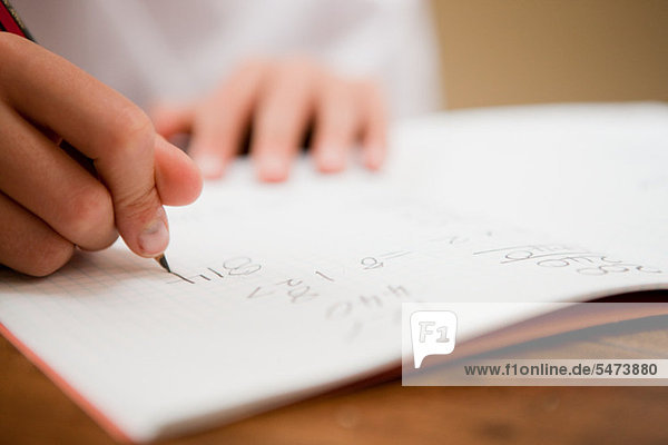 Close up of the hands of a young boy writing in a textbook