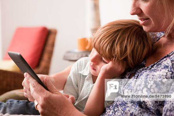 Sohn neben Mutter sitzt  während sie einen digitalen Tablet verwendet