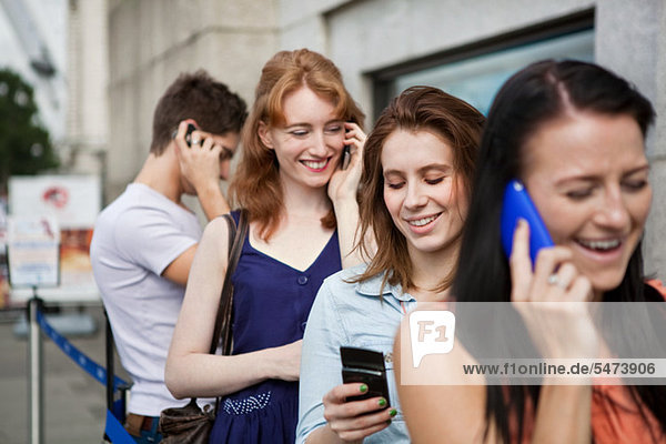 Four people in a queue  all using mobile phones