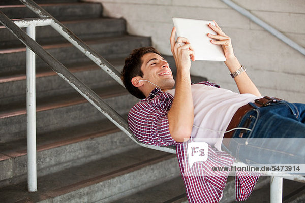 Junger Mann mit einen digitalen Tablet beim liegen auf einem Geländer