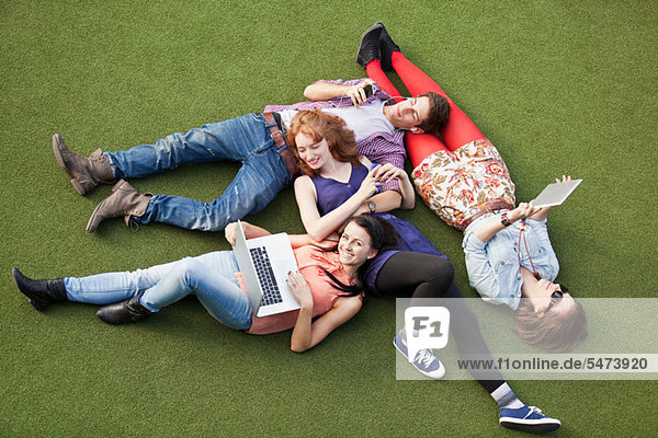 Vier Personen liegend mit Laptop  digitalem Tablett und Mobiltelefon