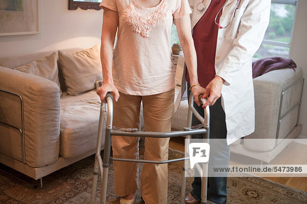 Arzt unterstützt ältere Frau auf dem Gehgestell