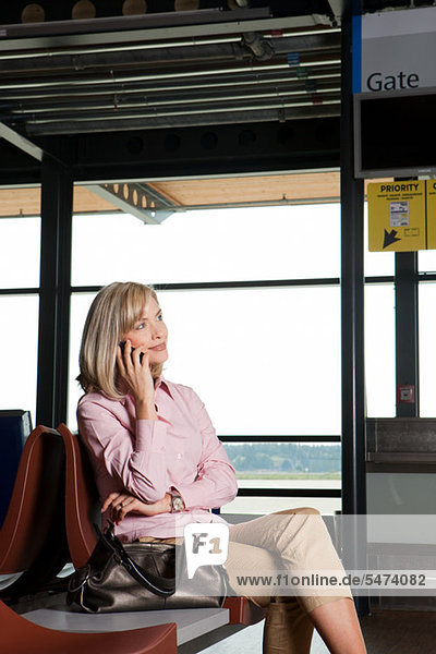Frau mittleren Alters am Telefon im Flughafen Abreise lounge