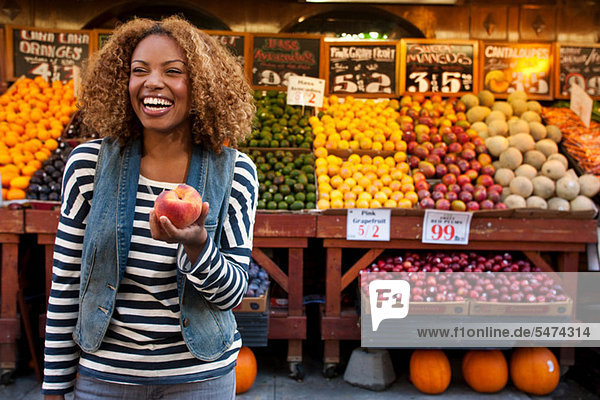 Junge Frau hält Pfirsich vom Marktstand  lächelnd