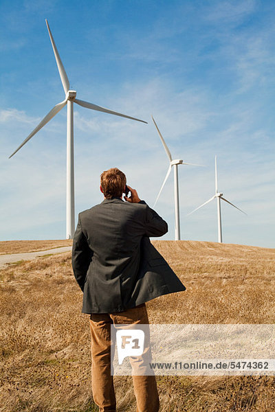 Man standing in front of wind turbines on mobile phone