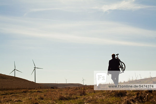 Man carrying bicycle up hill towards windfarm