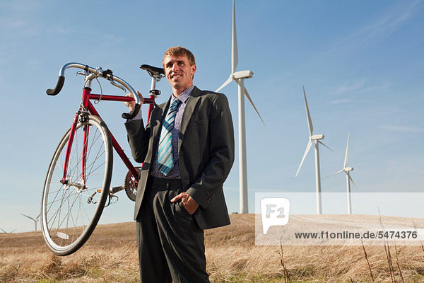 Man holding bicycle in front of wind turbines