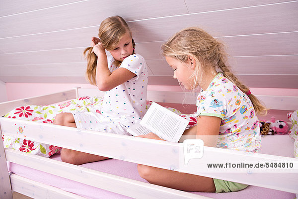Zwei Schwestern sitzen im Bett und lesen ein Buch